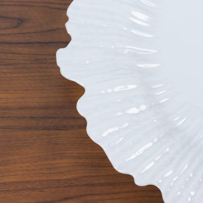 White decorative plate with scalloped edges on a wooden surface.
