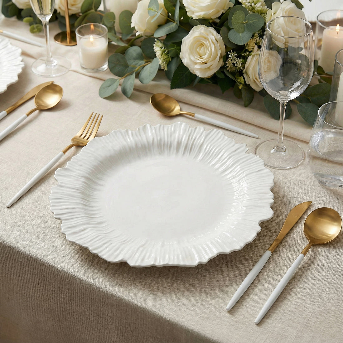 Elegant white plate with wavy edges, gold utensils, and floral centerpiece on a table.