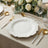 Elegant white plate with wavy edges, gold utensils, and floral centerpiece on a table.
