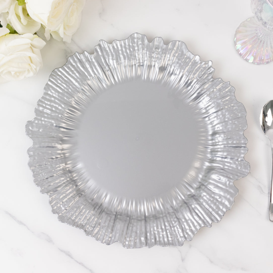 Silver decorative plate with a ruffled edge on a marble surface.
