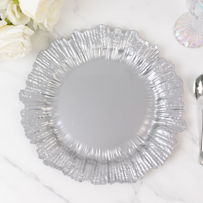 Silver decorative plate with a ruffled edge on a marble surface.