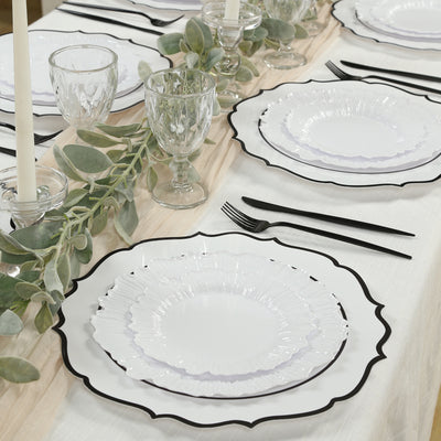 Elegant white plates with black trim set on a dining table with glassware and greenery.