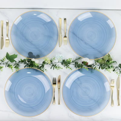 Four elegant blue plates with gold rims arranged with cutlery and greenery.