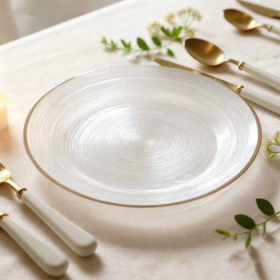 Elegant glass plate with gold rim, surrounded by cutlery and greenery.