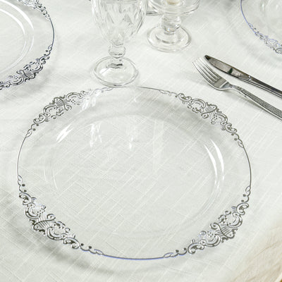 Elegant clear glass plate with ornate silver detailing on a textured table setting.