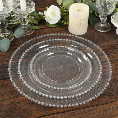 Set of elegant clear glass plates with beaded edges on wooden table.