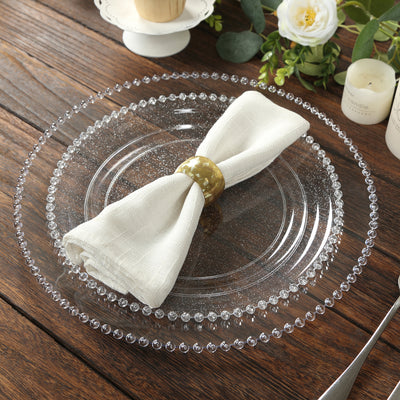 Clear decorative plate with a napkin and gold ring on a wooden table.