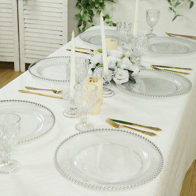 Elegant table setting with clear plates and glassware, adorned with candles and flowers.