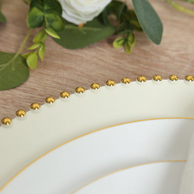Elegant white dinner plate with gold beaded rim on wooden table.