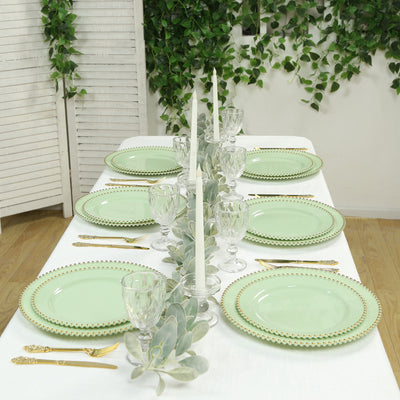 Elegant green dinner plates arranged on a table with candles and greenery.