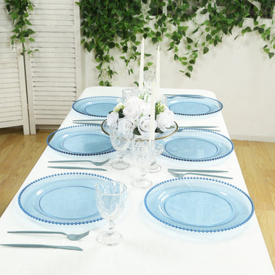 Elegant blue glass plates set on a dining table with floral centerpiece and candles.