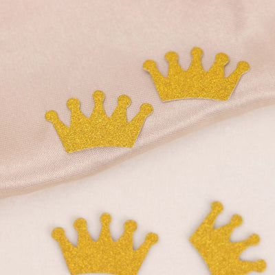 Gold glitter crown embellishments on soft fabric.