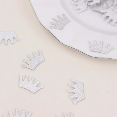Silver glitter crown confetti on a white plate and surface.