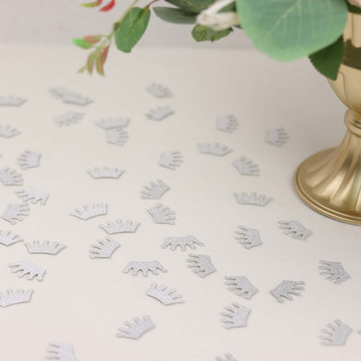 Scattered silver crown confetti on a light surface with a decorative vase.