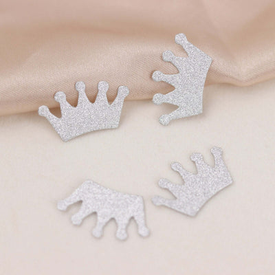 Glittery silver crown cutouts on a soft fabric background.