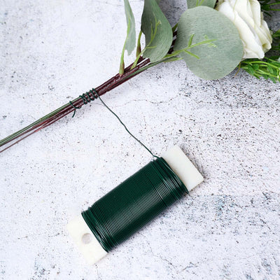 Green floral wire on a spool with a flower arrangement background.