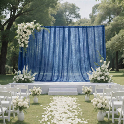Outdoor wedding ceremony setup with blue drapes, white flowers, and chairs