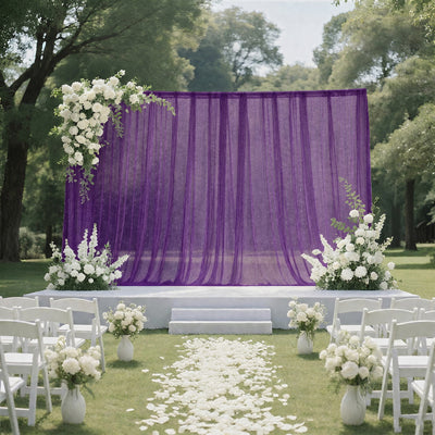 Outdoor wedding ceremony setup with purple backdrop, white flowers, and chairs