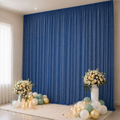 Elegant event backdrop with blue curtain, floral arrangements, candles, and balloons