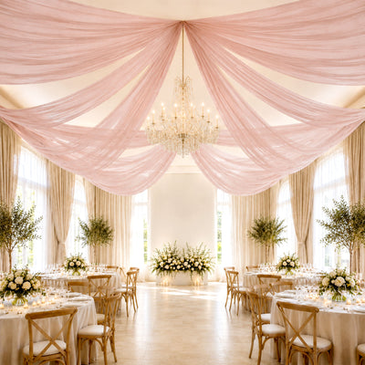 Elegant wedding reception hall with pink draped ceiling, chandelier, and floral tables