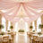 Elegant wedding reception hall with pink draped ceiling, chandelier, and floral tables