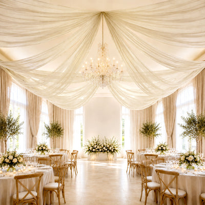 Elegant wedding reception hall with draped ceiling, chandelier, and floral tables