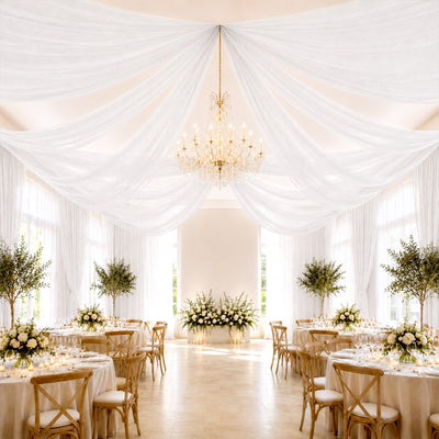 Elegant wedding reception with draped white ceiling, chandelier, and floral tables