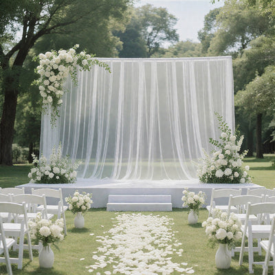 Elegant outdoor wedding altar with floral arrangements and sheer drapery.