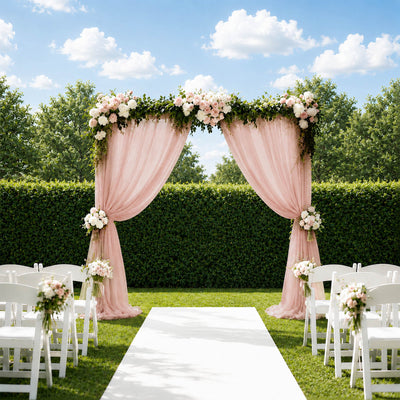 Outdoor wedding arch with pink drapes, flowers, and white chairs on a sunny lawn