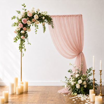 Elegant blush pink floral wedding arch with draped fabric and candles