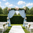 Outdoor wedding ceremony arch with blue drapes, flowers, and white chairs