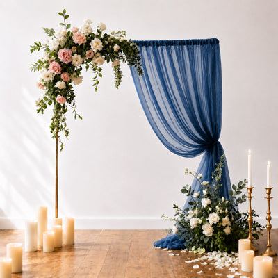 Elegant floral wedding arch with blue drapery, candles, and white roses