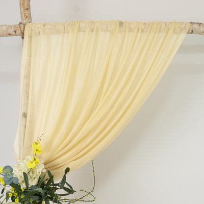 Soft yellow draped fabric with floral arrangement on a natural branch backdrop.