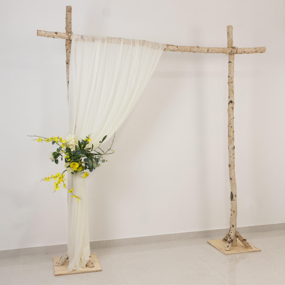 Rustic birch wedding arch with white drapes and yellow floral arrangement