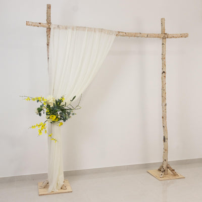 Rustic birch wedding arch with white drapes and yellow floral arrangement