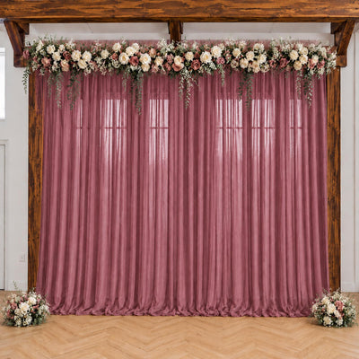 Pink wedding backdrop with floral garland, draped curtains, and wooden arch