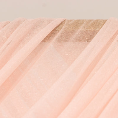 Sheer pink fabric draping elegantly on a wooden surface.