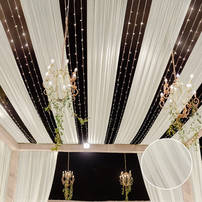 Elegant draped ceiling with chandeliers and fairy lights in a festive setting.
