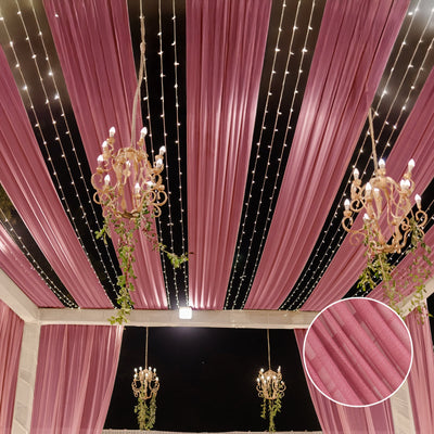 Elegant pink drapery with chandeliers and fairy lights in a festive setting.