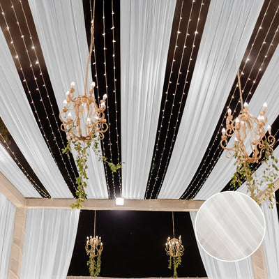 Elegant draped ceiling with chandeliers and fairy lights in a festive setting.