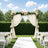 Outdoor wedding ceremony arch with white drapes, pink roses, and garden seating
