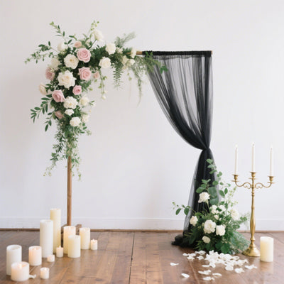 Elegant wedding arch with roses and drapery, surrounded by candles and decor.