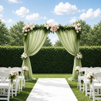 Outdoor wedding arch with green drapes, blush flowers, and white chairs in a garden