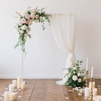 Floral wedding arch with drapery and candles on a wooden floor.