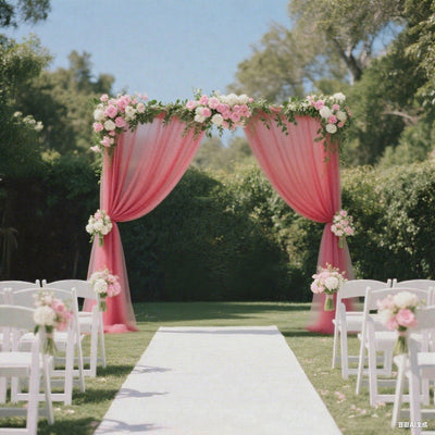 Pink floral wedding arch with draped fabric in a garden setting.