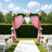 Pink floral wedding arch with white chairs and aisle in outdoor garden ceremony