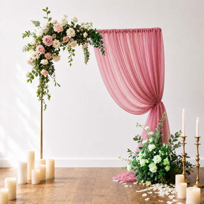 Pink floral wedding backdrop with roses, draped chiffon, candles, and greenery
