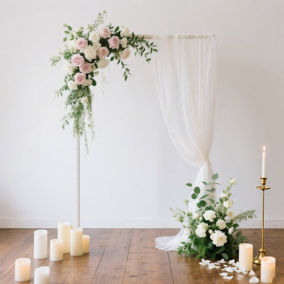Wedding arch with flowers, drapery, and candles in a serene setting.