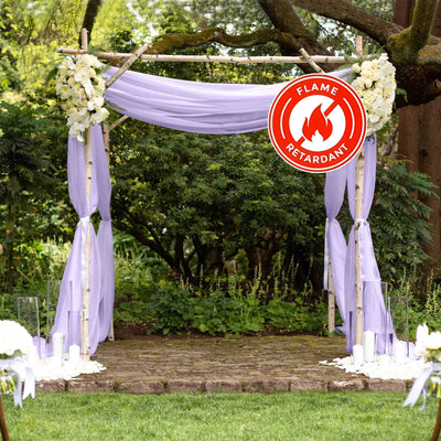 Wedding arch with lavender drapes and white floral decorations in a garden setting.