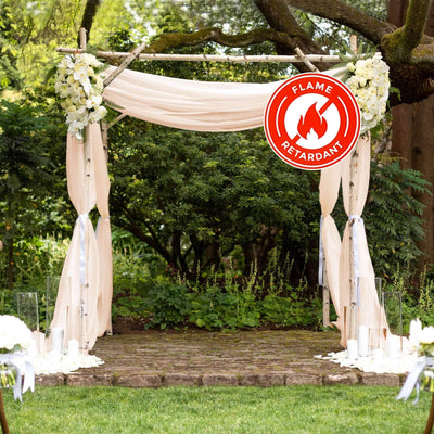 Wedding arch adorned with white flowers and draped fabric, marked as flame retardant.
